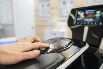 Nahaufnahme einer Hand, die Tasten auf einem eleganten, modernen Bedienfeld drückt und damit eine Anwendung auf einem Bildschirm im Hintergrund steuert.