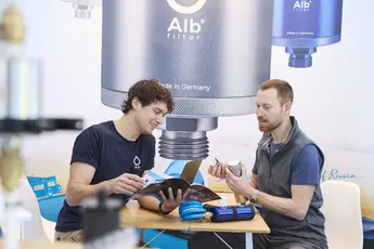 Zwei Personen befinden sich an einem Messestand zum Thema Wasserfilter in einem Verkaufsgespräch.