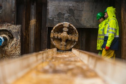 Zwei Arbeiter in Schutzkleidung inspizieren eine große Tunnelbohrmaschine auf einer Baustelle.