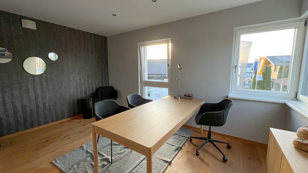 Minimalistisches Büro mit Holzschreibtisch, schwarzen Stühlen, großen Fenstern und hellem Holzfußboden.