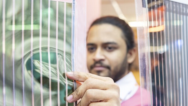 Ein Mann prüft mit konzentriertem Gesichtsausdruck eine aufgehängte Folie mit integrierten Schaltkreisen oder Solarmodulen.