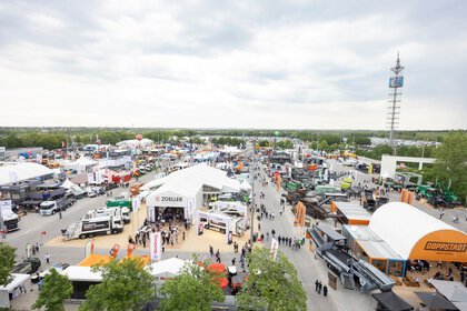 Weitwinkelansicht eines großen Freigeländes einer Fachmesse mit vielen Ständen, Nutzfahrzeugen, Maschinen und zahlreichen Besuchern zwischen den Ausstellungsbereichen