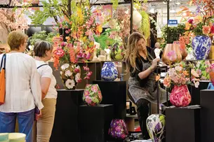 Auf der TrendSet arrangiert eine Floristin kunstvoll bunte Vasen, während zwei Frauen die lebendigen Blumenarrangements bewundern.