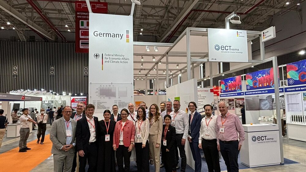 Several smiling individuals in suits pose for a group photo in front of a stand belonging to the Federal Ministry for Economic Affairs and Climate Action.