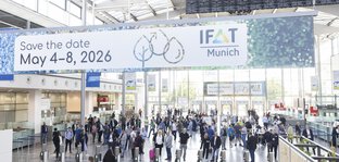 Crowd in the entrance hall of the trade fair. In focus is a sign hanging from the ceiling with the inscription “IFAT Munich: Save the date May 4-8, 2026”
