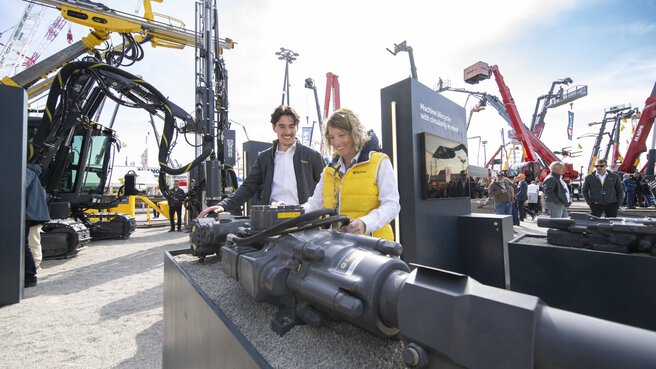 A man and a woman look at a black technical device at a trade fair.