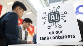 Menschen stehen neben einem Schild mit einem Schaltkreis und dem Text „KI auf unseren Tankcontainern“.