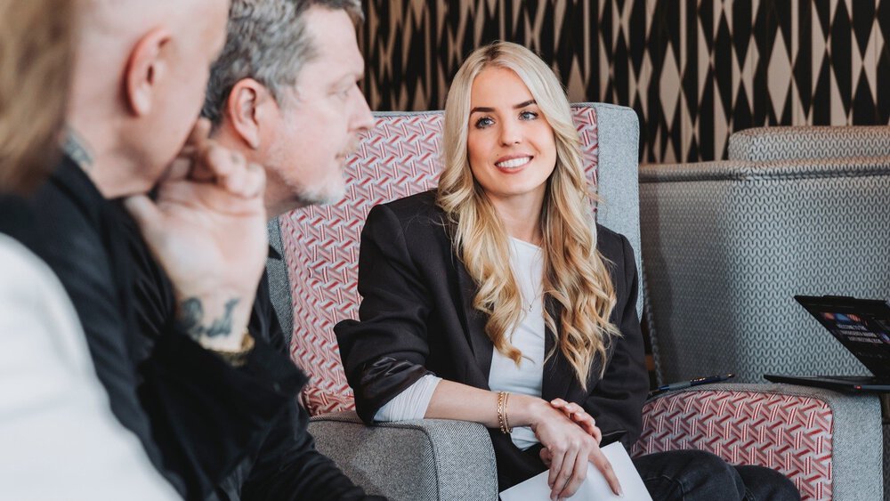 Two women and two men are sitting together on upholstered furniture in a colorfully decorated corner, looking at each other.