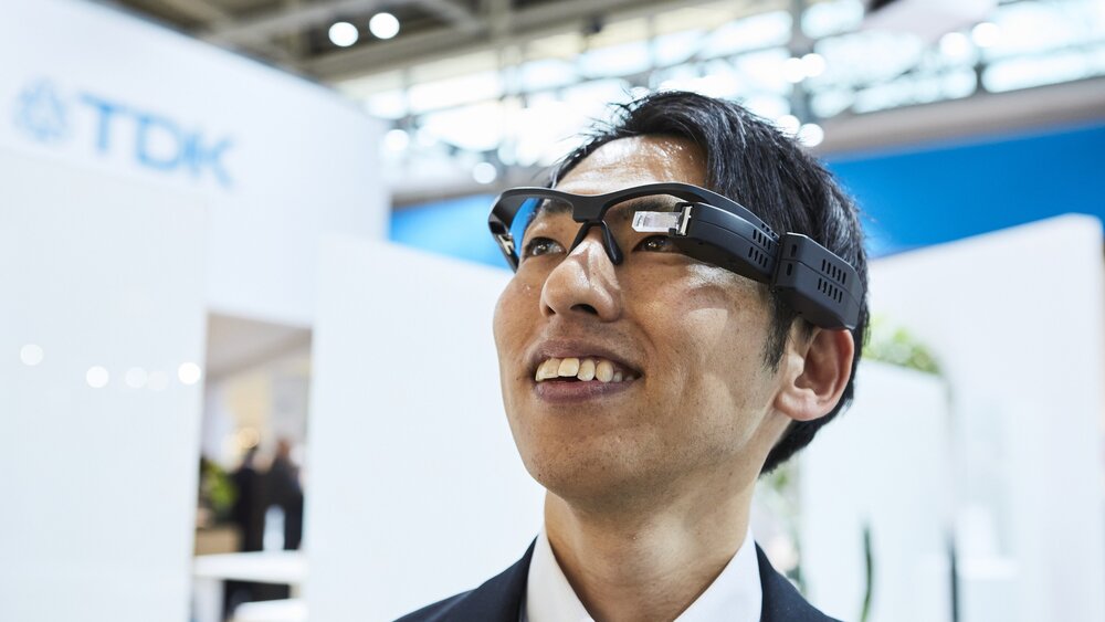 Smiling person with data glasses, exhibition stands in the background.