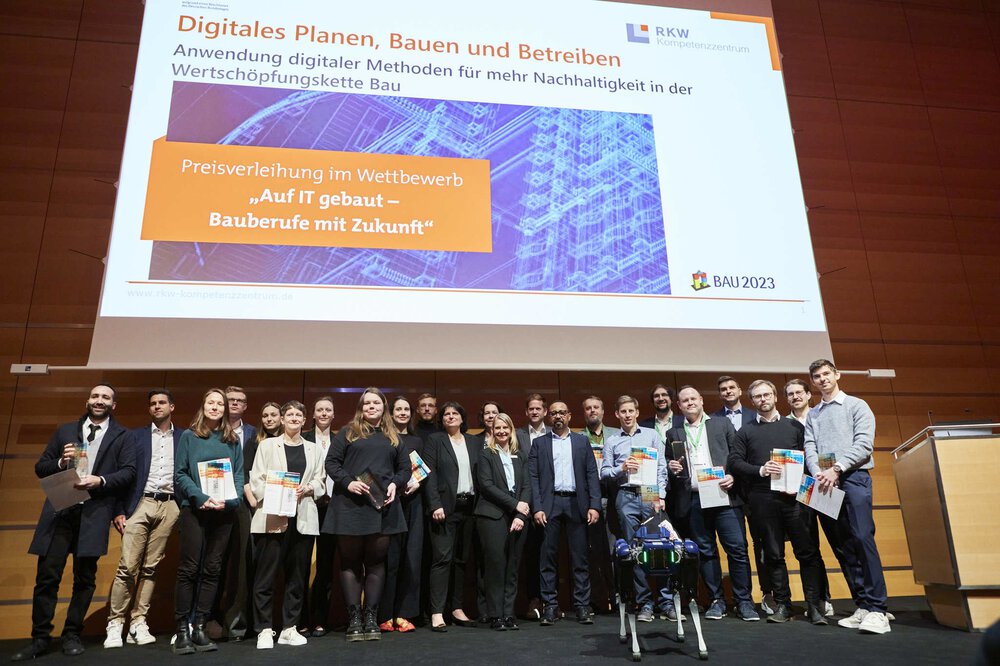 Die Gewinner des Wettbewerbs „Auf IT gebaut - Bauberufe mit Zukunft“ posieren mit ihren Preisen und Urkunden auf einer Bühne für ein Foto.