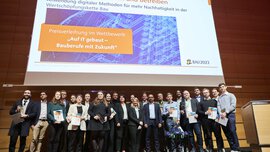 Die Gewinner des Wettbewerbs „Auf IT gebaut - Bauberufe mit Zukunft“ posieren mit ihren Preisen und Urkunden auf einer Bühne für ein Foto.
