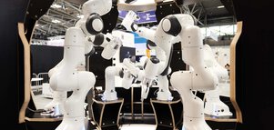 A group of white robot arms arranged in a circular formation at an exhibition stand.