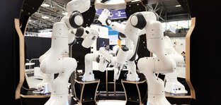 A group of white robot arms arranged in a circular formation at an exhibition stand.