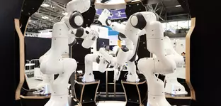 A group of white robot arms arranged in a circular formation at an exhibition stand.