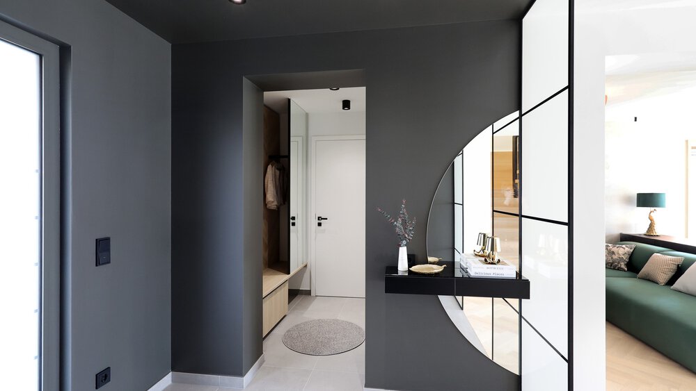 Ein moderner grauer Flur in kantigem Design mit Blick auf die Haustür. Rechts geht es in den Wohnbereich.