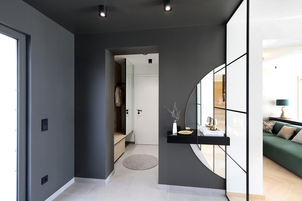 Ein moderner grauer Flur in kantigem Design mit Blick auf die Haustür. Rechts geht es in den Wohnbereich.