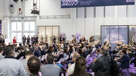 Ein Publikum aus sitzenden und stehenden Menschen während einer Präsentation im Forum Halle 1 auf der digitalBAU.
