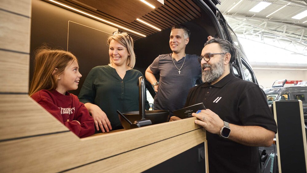 Eine Familie besichtigt einen Campervan auf der Messe f.re.e und unterhält sich mit einem Aussteller über die Innenausstattung.