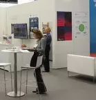 Trade fair visitors gathered at tables at an exclusive stand, surrounded by colorful posters and a screen adorning the walls.