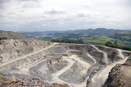 A large open-cast mine with terraced plains, surrounded by green hills and clouds in the sky.