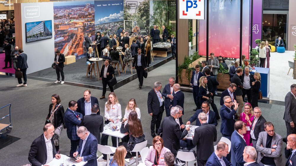 A view of several busy exhibition stands and visitors in the aisles between them. A large white sign bears the letters ‘P3’ in red brackets.