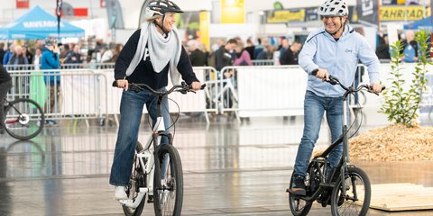 Ein Mann und eine Frau mit Helmen sitzen lachend je auf einem Fahrrad und testen diese auf einer abgetrennten Fläche auf der f.re.e aus.