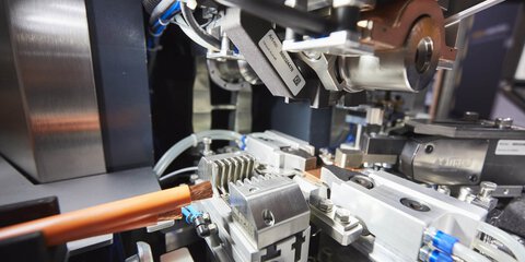 Nahaufnahme einer komplexen Industriemaschine mit metallischen Komponenten und einem orangefarbenen Kabel während der productronica.