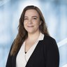 Portrait einer Frau mit langen braunen Haaren, einem schwarzen Blazer und einer weißen Bluse.