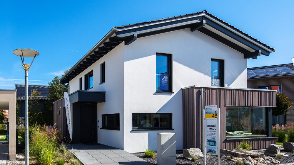 Modernes zweistöckiges Haus mit Sonnenkollektoren, weißen Wänden und schwarzen Akzenten vor einem klaren blauen Himmel.