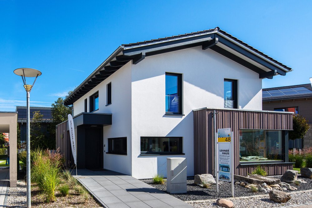 Modernes zweistöckiges Haus mit Sonnenkollektoren, weißen Wänden und schwarzen Akzenten vor einem klaren blauen Himmel.