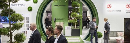 Ein großer runder grüner Durchgang in der Wand eines Messestandes auf der BAU, an dem einige Leute vorübergehen und andere sich unterhalten.