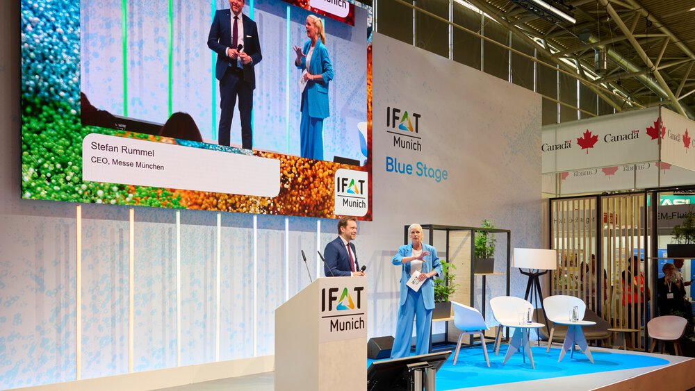 Moderation auf der IFAT Munich Blue Stage mit zwei Personen am Podium, großem Bildschirm und sichtbarem Namenseinblendung „Stefan Rummel, CEO, Messe München“.