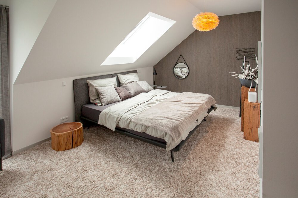 Ein gemütliches Schlafzimmer im Dachgeschoss mit Oberlicht, dunklem Bettgestell, grauer Akzentwand und Holzkommode.