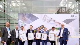 Eine Gruppe von Menschen mit Auszeichnungen steht vor einer Messehalle und einem Plakat der World of Photonics.