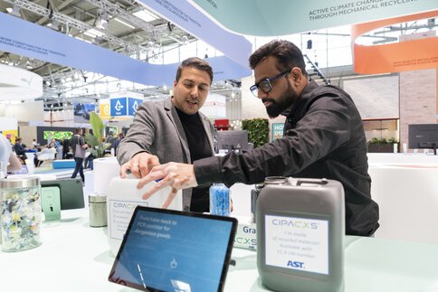 A man presents a PCR canister system to a visitor at a trade fair stand.