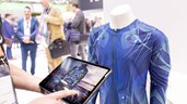 Person holding tablet with a music selection menu in front of a mannequin wearing a tight-fitting, blue patterned top on which LEDs are shining.