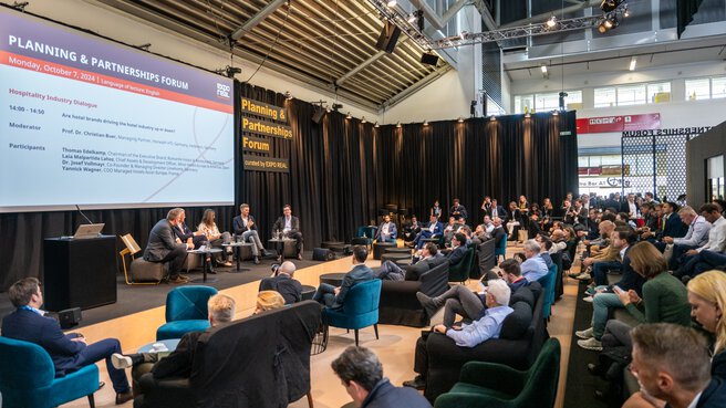 Five people at a panel discussion in a conference area of an exhibition hall. On the stage it says 