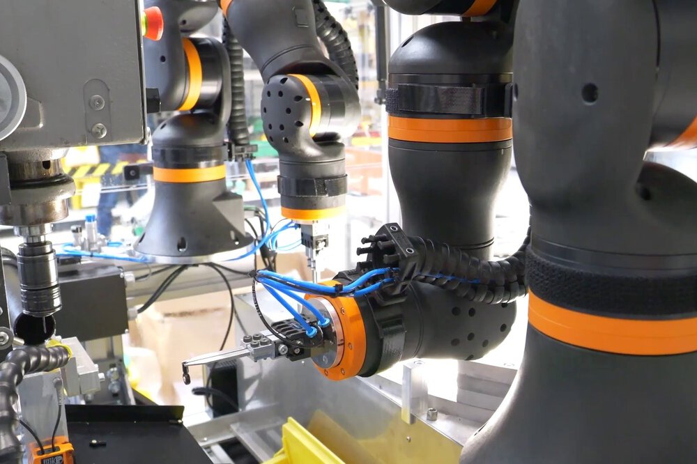Close-up of several black and orange robot arms working with precision tools.
