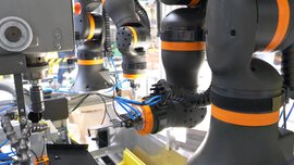 Close-up of several black and orange robot arms working with precision tools.