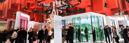 Blick auf einen Messestand der BAU mit Fokus auf die Hallendecke, an der zahlreiche rote Quader und Quaderrahmen in verschiedenen größen hängen.