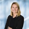 Lächelnde Frau mit schulterlangem blondem Haar in einem schwarzen Blazer und schwarzem Shirt.