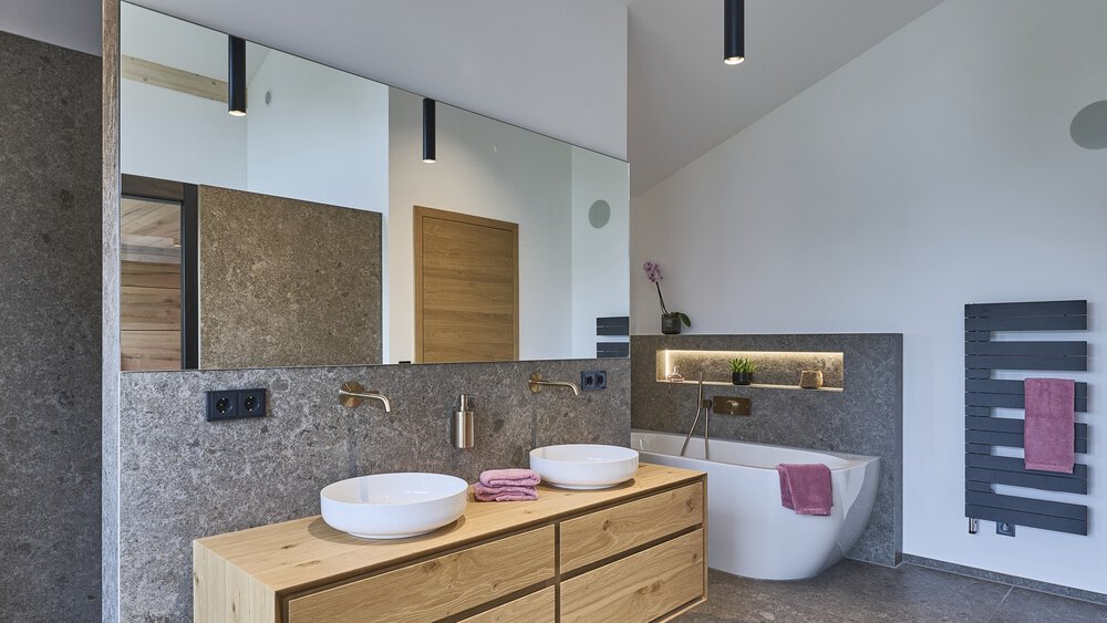 Modernes Badezimmer mit Doppelwaschbecken, großem Spiegel, freistehender Badewanne und dunklen Akzenten in minimalistischem Design.