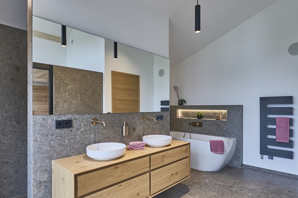 Modernes Badezimmer mit Doppelwaschbecken, großem Spiegel, freistehender Badewanne und dunklen Akzenten in minimalistischem Design.
