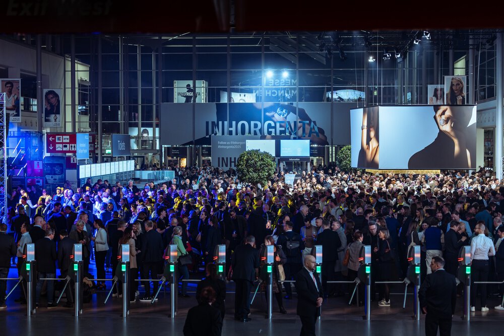 Eine große Menschenmenge versammelt sich am Eingang einer Indoor-Veranstaltung mit heller Beleuchtung und digitalen Bildschirmen.