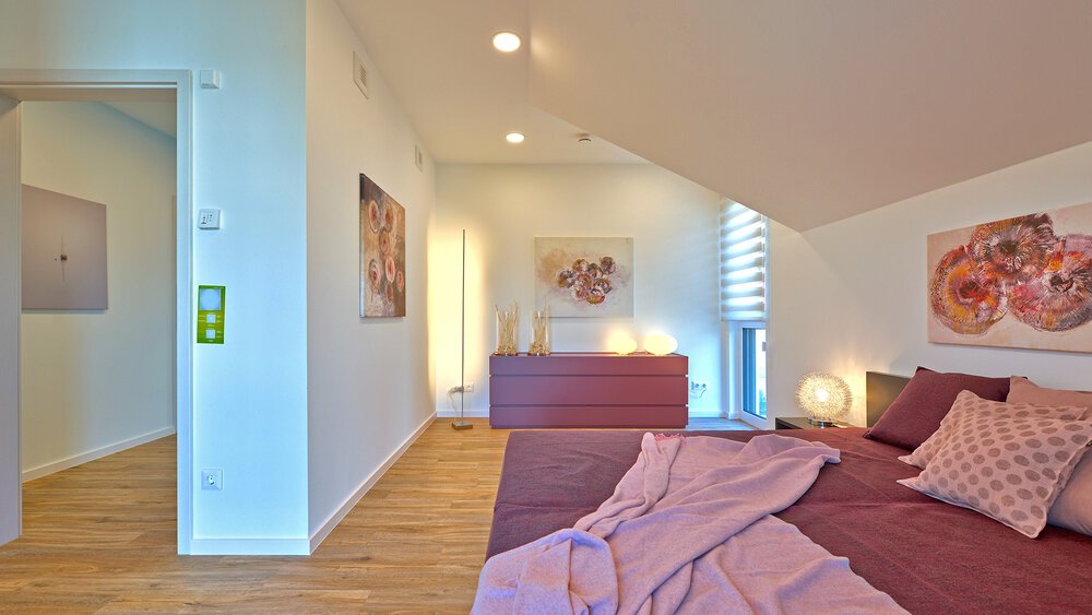 Ein helles Schlafzimmer mit rosa Bettwäsche, moderner Kunst an den Wänden und einer offenen Tür, die zu einem Flur führt.
