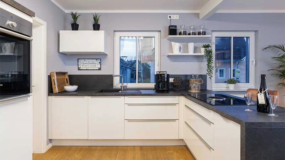 Moderne Küche mit weißen Schränken, schwarzen Arbeitsplatten, einem Fenster und verschiedenen Geräten auf den Arbeitsplatten.