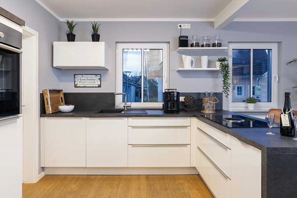 Moderne Küche mit weißen Schränken, schwarzen Arbeitsplatten, einem Fenster und verschiedenen Geräten auf den Arbeitsplatten.