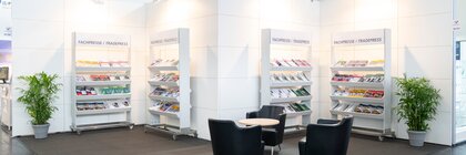 Exhibition stand with chairs, table and shelves displaying trade press magazines.