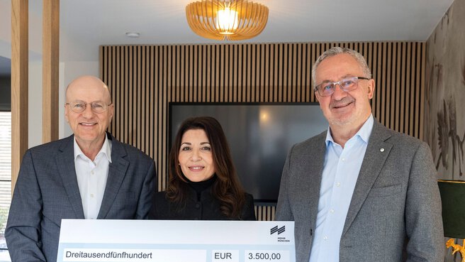 Drei lächelnde Menschen, die einen großen Spendenscheck über 3.500 Euro für einen inklusiven Spielplatz in der Hand halten.