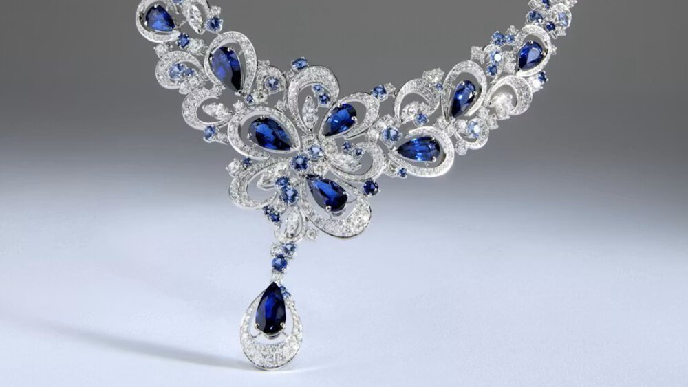 Close-up of a delicate silver necklace with numerous dark blue teardrop-shaped gemstones set into it.